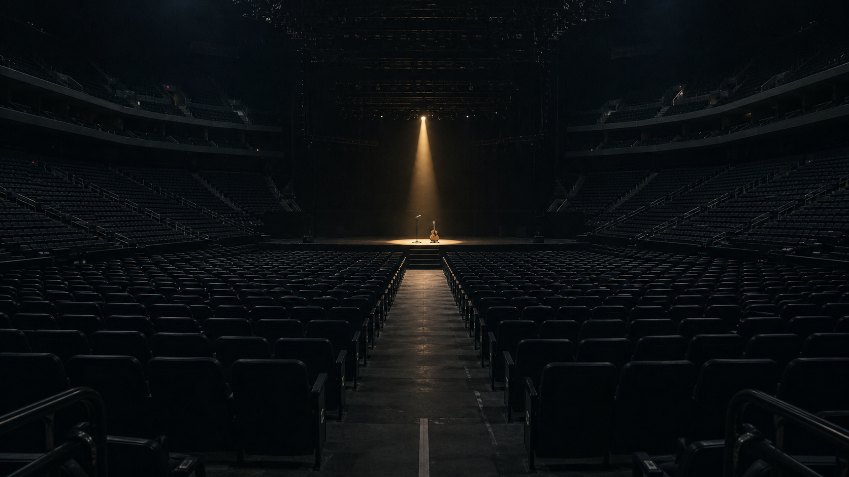 A completely empty arena faces a stage with one spotlight, microphone, and guitar.